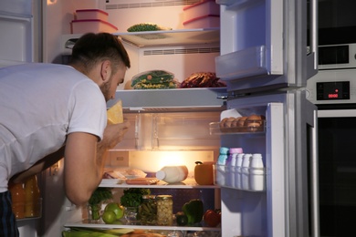Photo of Young man looking for food in refrigerator at night