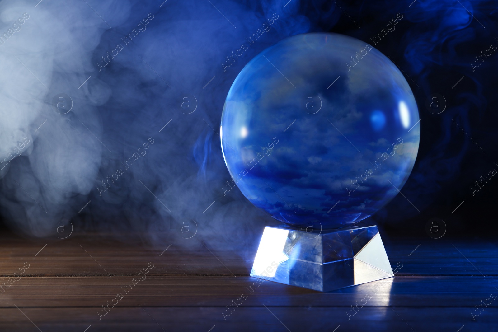 Photo of Magic crystal ball on wooden table and smoke against dark background, space for text. Making predictions