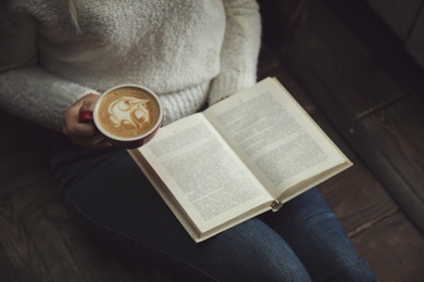 Photo of Woman with cup of coffee reading book at home, closeup