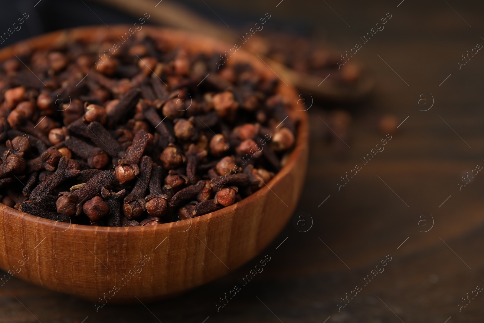 Photo of Aromatic cloves in bowl on wooden table, closeup. Space for text