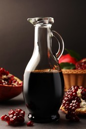Photo of Glass jug of tasty pomegranate sauce and fresh ripe fruits on light grey table