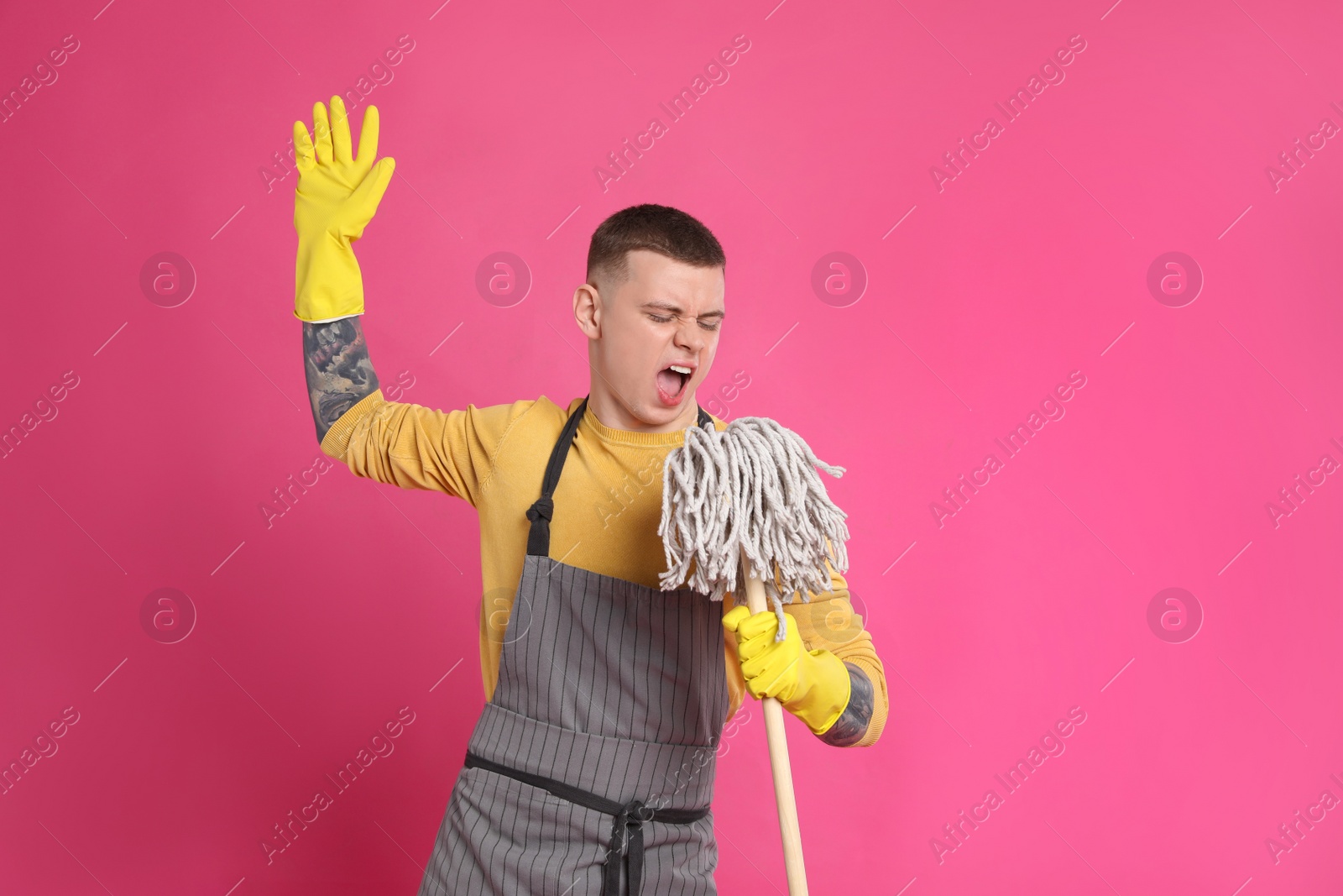 Photo of Handsome young man with mop singing on pink background