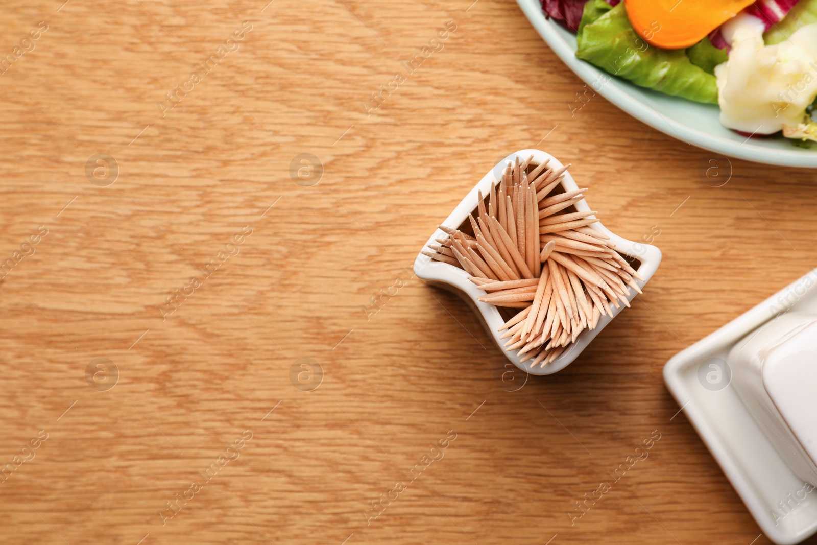 Photo of Holder with many toothpicks near food on wooden table, flat lay. Space for text