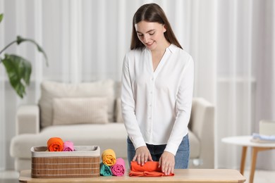 Smiling woman rolling shirt at table in room. Organizing clothes