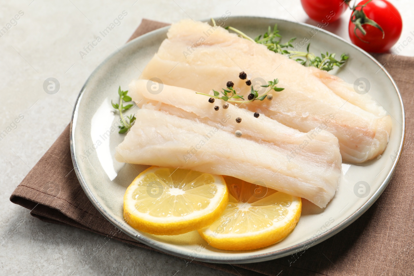 Photo of Plate with raw cod fish, spices, microgreens and lemon on grey table, closeup