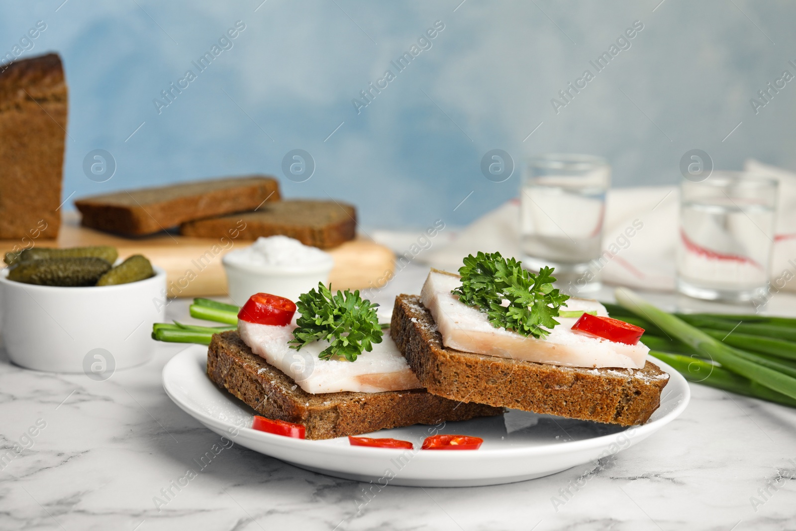 Photo of Composition with plate of pork fatback sandwiches on marble table against blue background