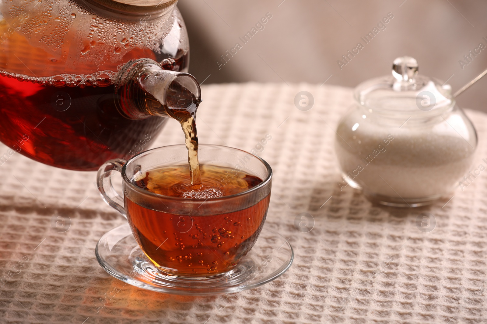 Photo of Pouring aromatic tea into cup at table, closeup