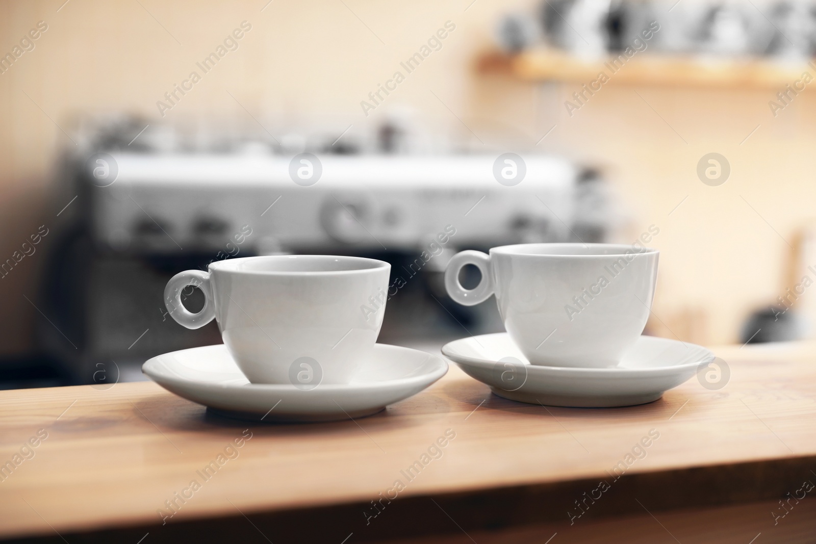 Photo of Cups of fresh aromatic coffee on table against blurred background