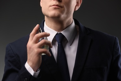 Handsome man in suit using perfume on dark background, closeup