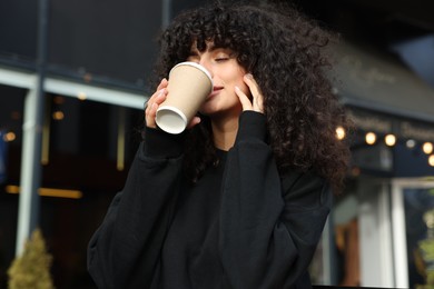 Photo of Young woman in stylish black sweater drinking coffee outdoors