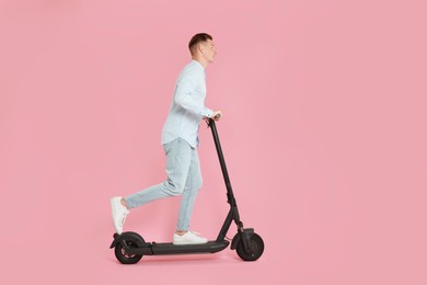 Young man riding modern electric kick scooter on pink background