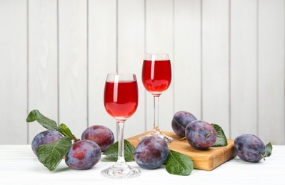 Photo of Delicious plum liquor and ripe fruits on table against white background. Homemade strong alcoholic beverage