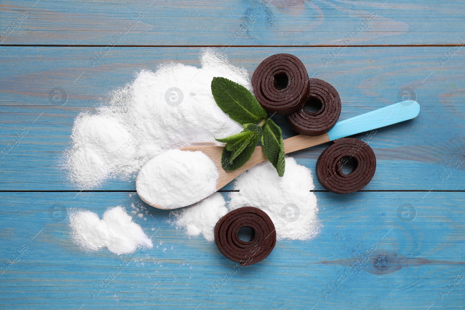 Photo of Sweet fructose powder, mint leaves and fruit leather rolls on light blue wooden table, flat lay