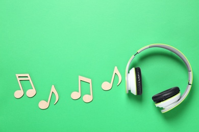 Photo of Wooden music notes and headphones on green background, flat lay