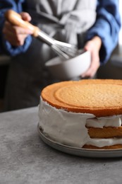 Woman decorating delicious homemade layer cake with cream at grey table, closeup