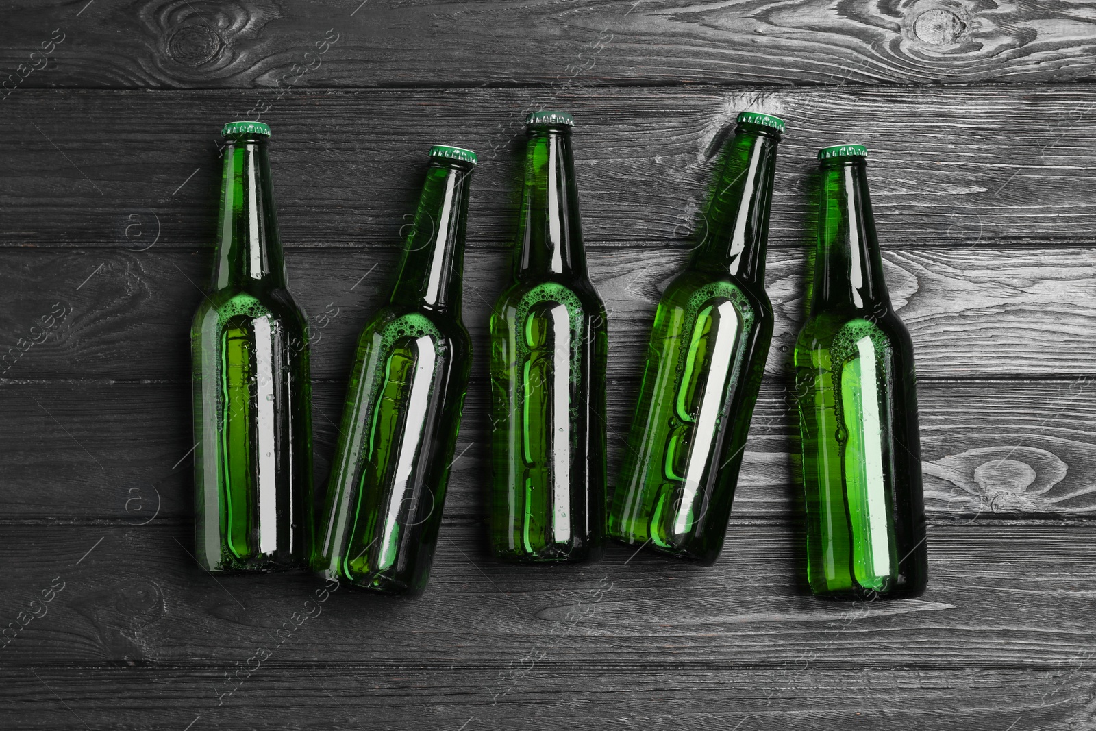 Photo of Glass bottles of beer on black wooden background, flat lay