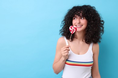 Beautiful woman with lollipop on light blue background, space for text