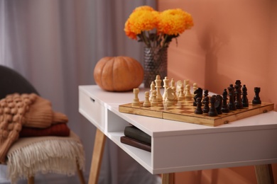 Chess board with pieces on white table in room. Cozy interior inspired by autumn colors