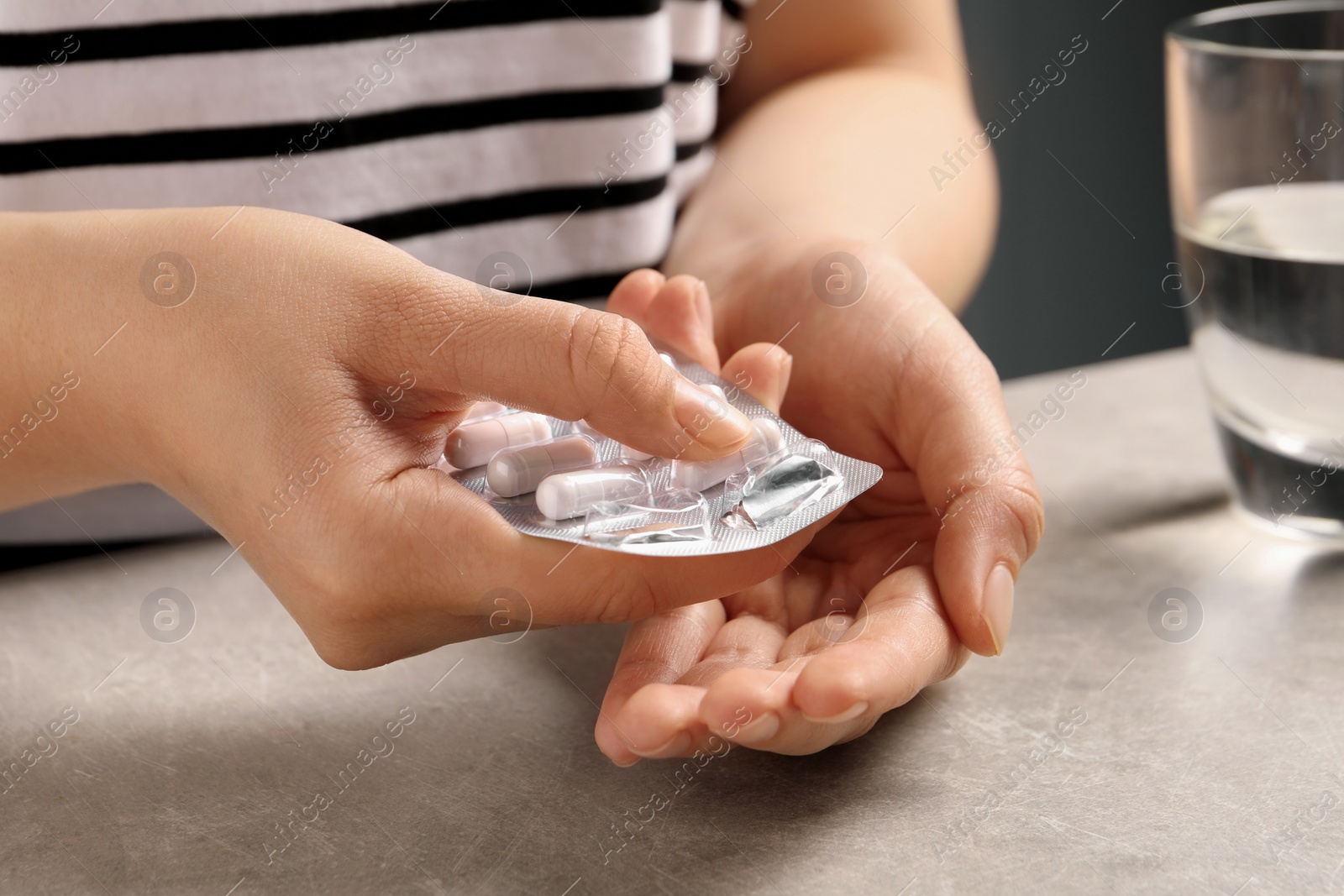 Photo of Woman taking pill out from blister pack at grey table, closeup