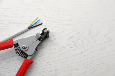 Photo of Professional cutters and cable with stripped wire on white wooden table, above view. Space for text
