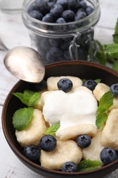 Bowl of tasty lazy dumplings with blueberries, sour cream and mint leaves on table, closeup