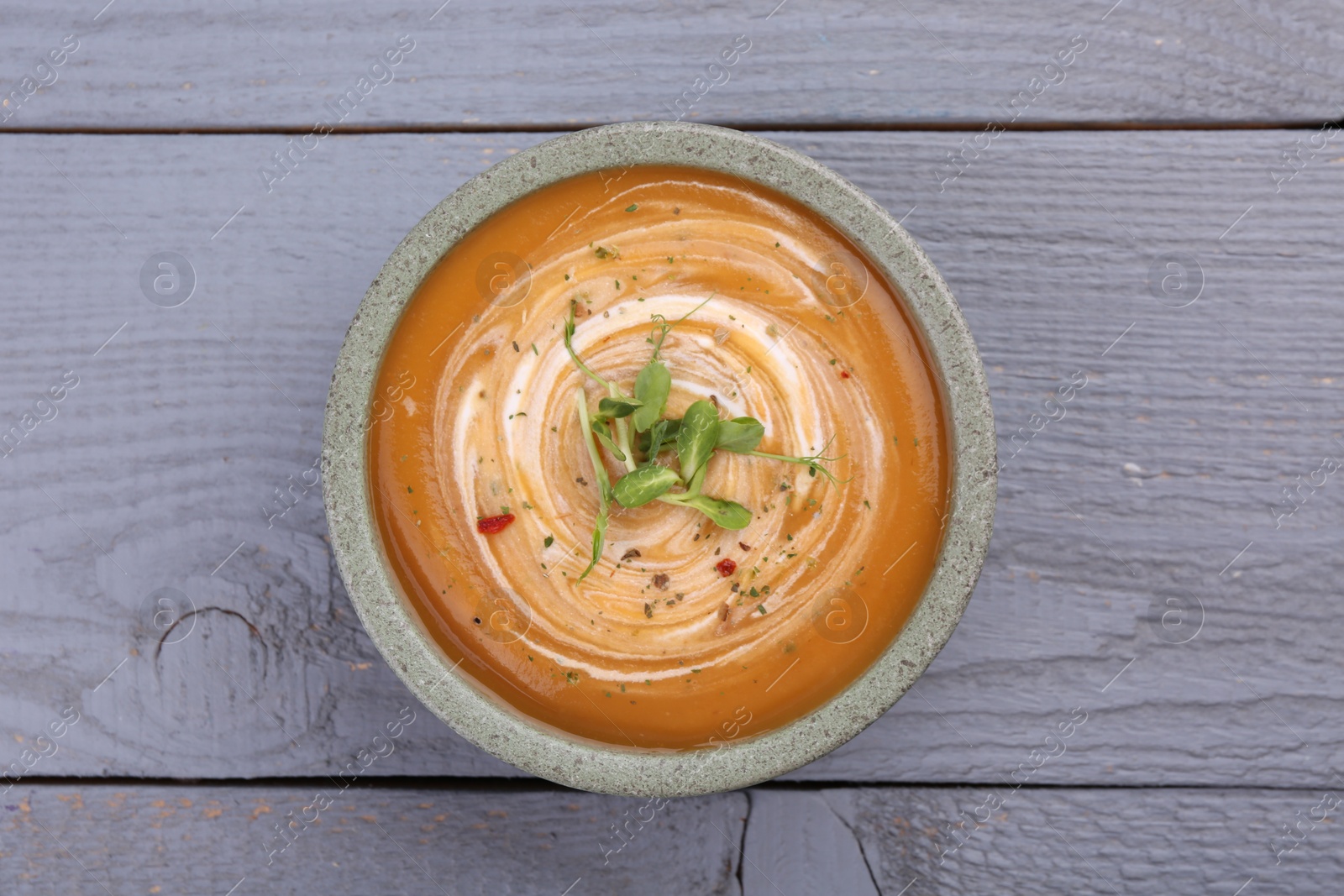 Photo of Delicious pumpkin soup with microgreens in bowl on gray wooden table, top view