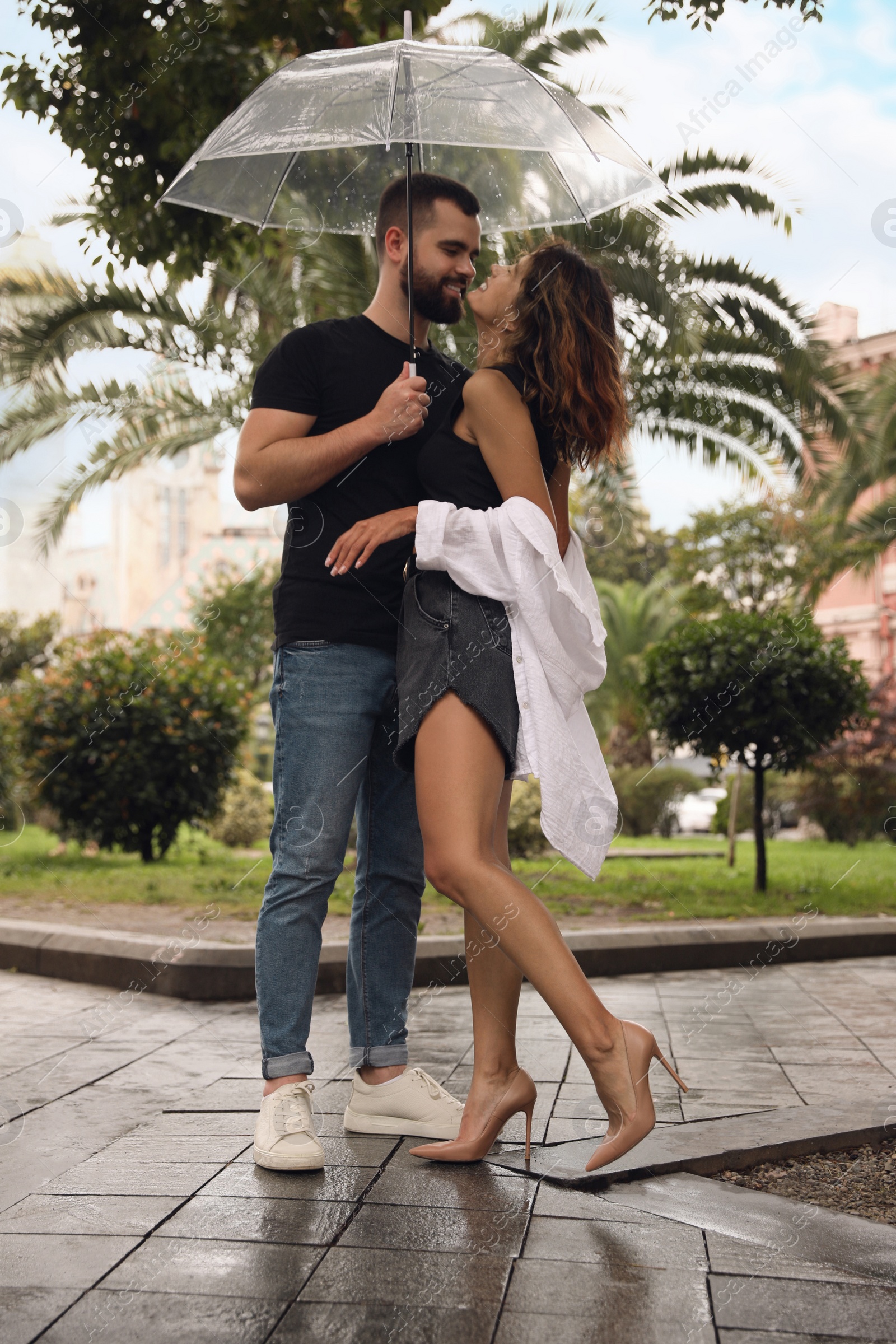 Photo of Young couple with umbrella enjoying time together under rain on city street