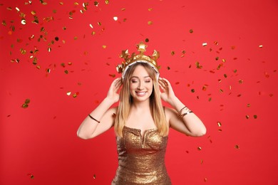 Happy young woman in party crown and confetti on red background