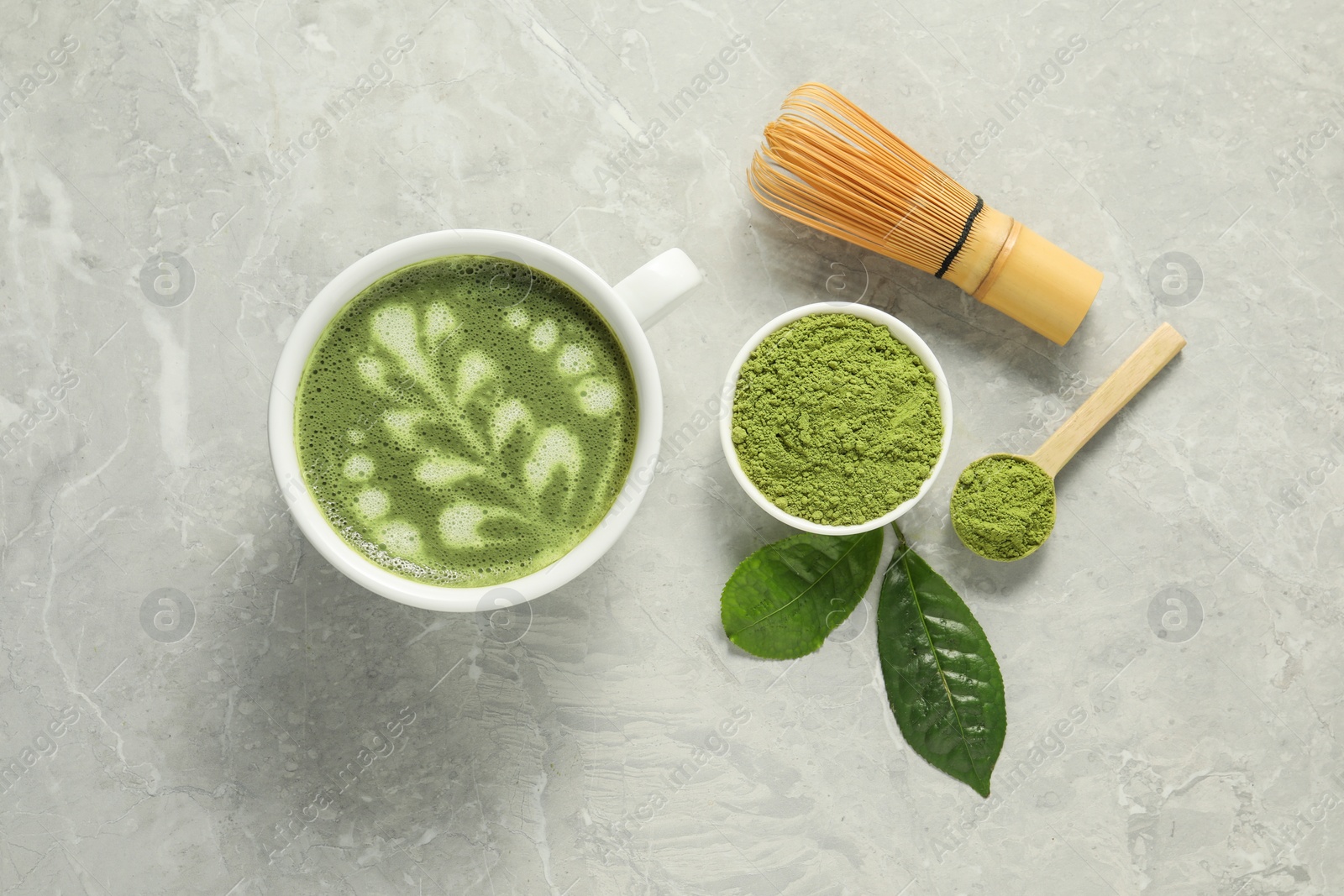 Photo of Delicious matcha latte, powder, leaves and whisk on grey textured table, flat lay