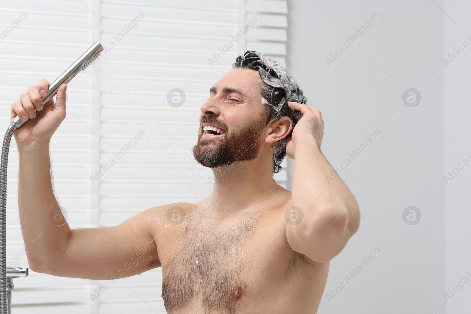 Photo of Happy man washing his hair with shampoo in shower