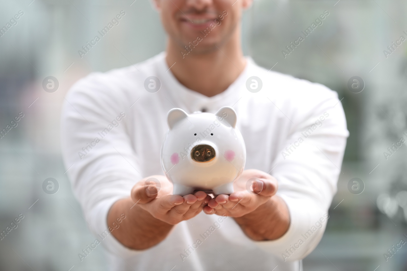 Photo of Man holding white piggy bank against blurred background, closeup