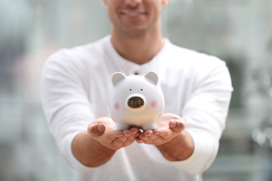 Man holding white piggy bank against blurred background, closeup