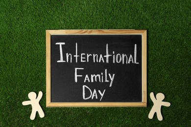 Photo of Chalkboard with text International Family Day and wooden figures on green grass, flat lay