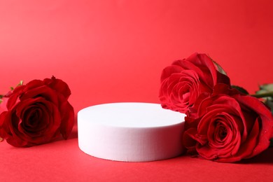 Photo of Stylish presentation for product. Round podium and beautiful roses on red background, space for text
