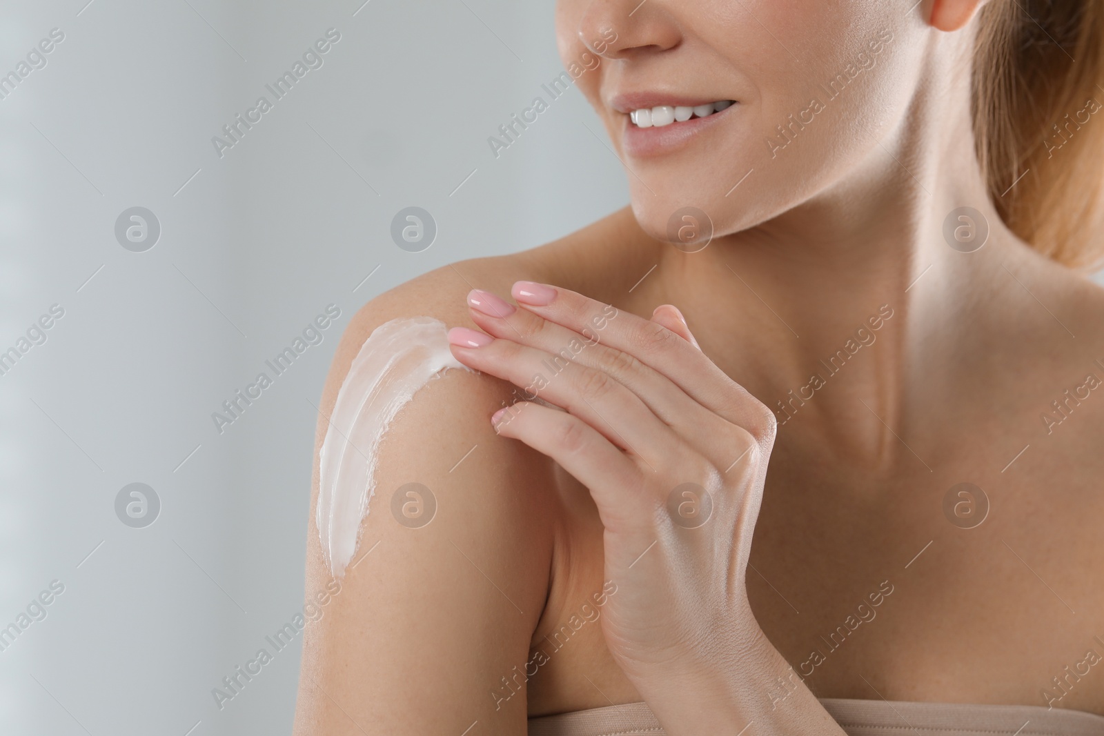 Photo of Woman applying body cream onto shoulder on light grey background, closeup. Space for text