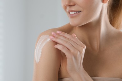 Woman applying body cream onto shoulder on light grey background, closeup. Space for text