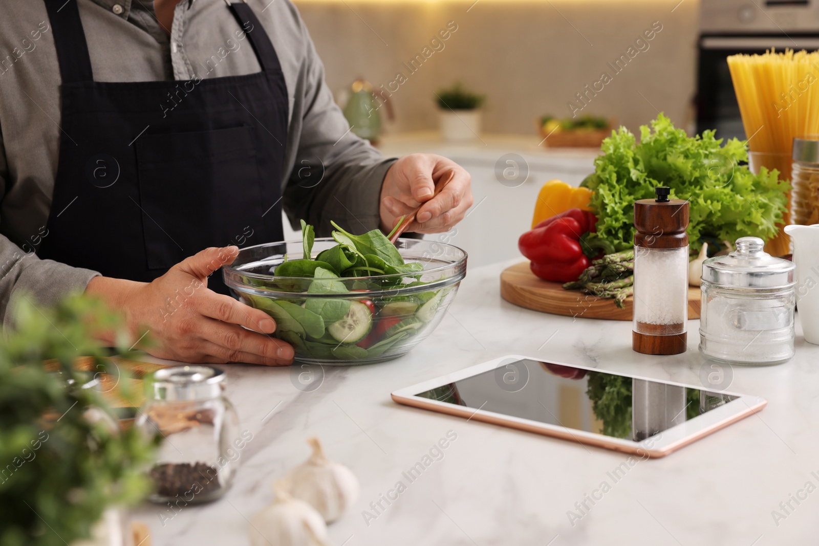 Photo of Man cooking salad at white marble countertop in kitchen, closeup