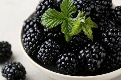 Photo of Bowl of fresh blackberries with leaves on table, closeup