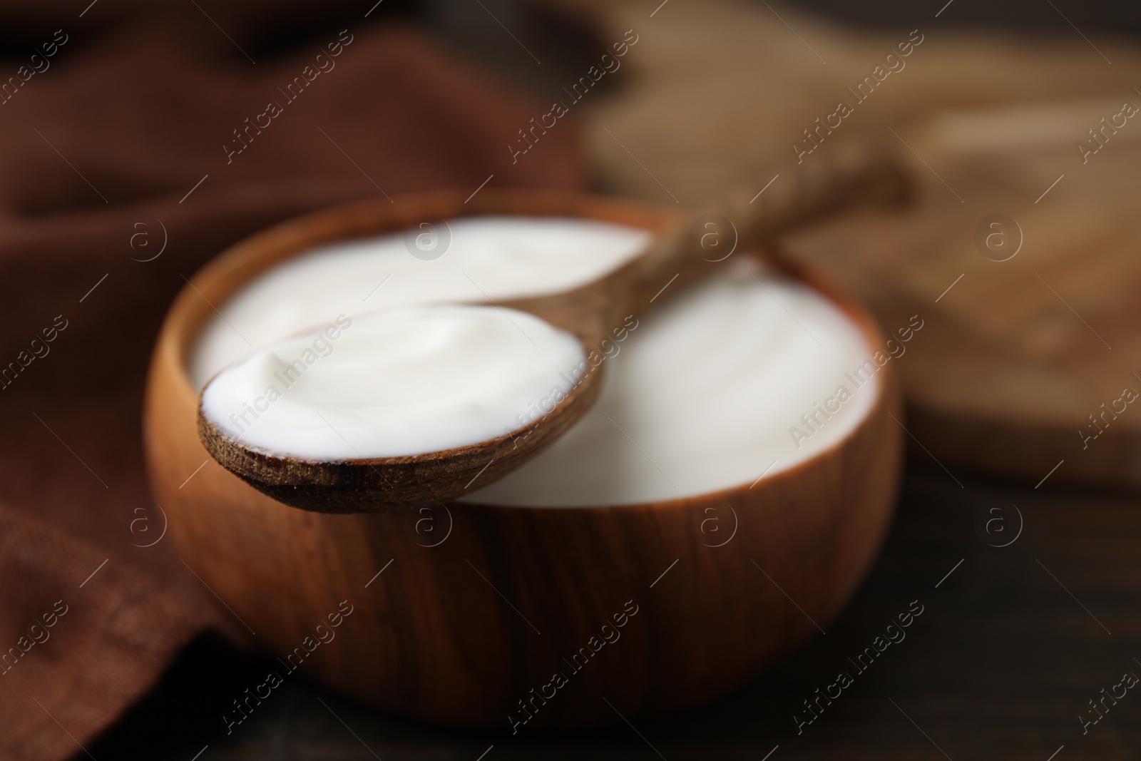 Photo of Delicious natural yogurt in bowl and spoon on wooden table, closeup