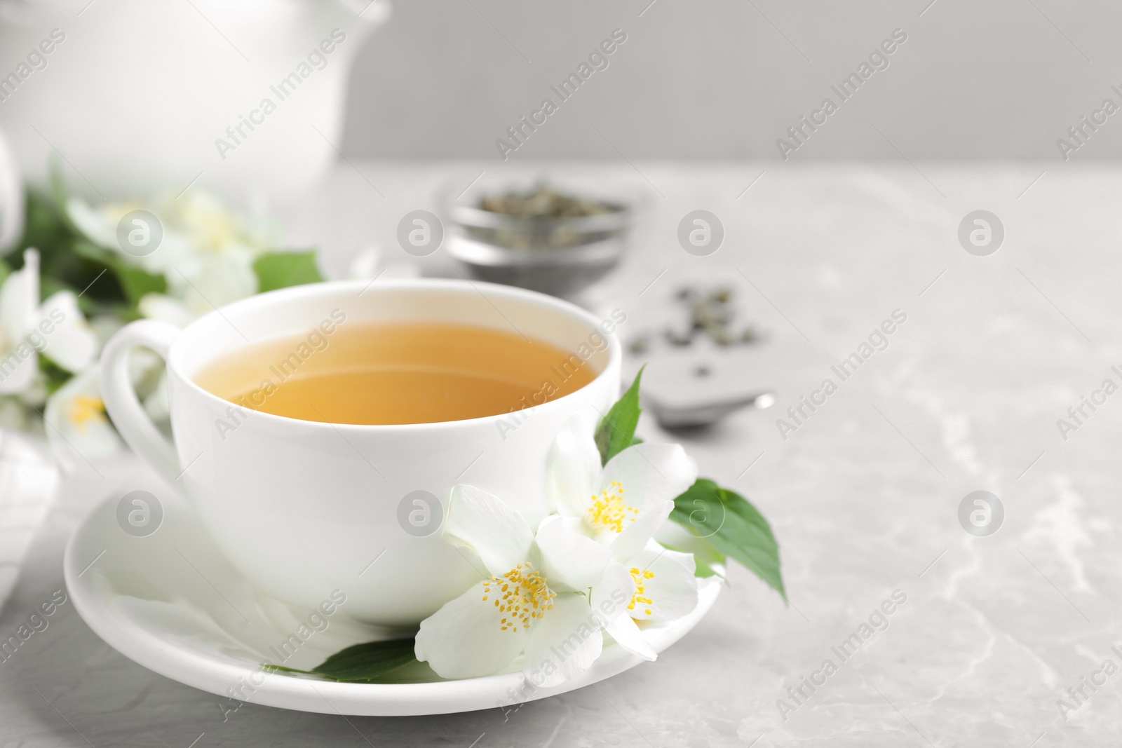 Photo of Cup of tea and fresh jasmine flowers on light grey marble table. Space for text