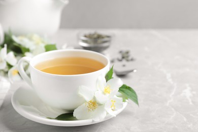 Photo of Cup of tea and fresh jasmine flowers on light grey marble table. Space for text
