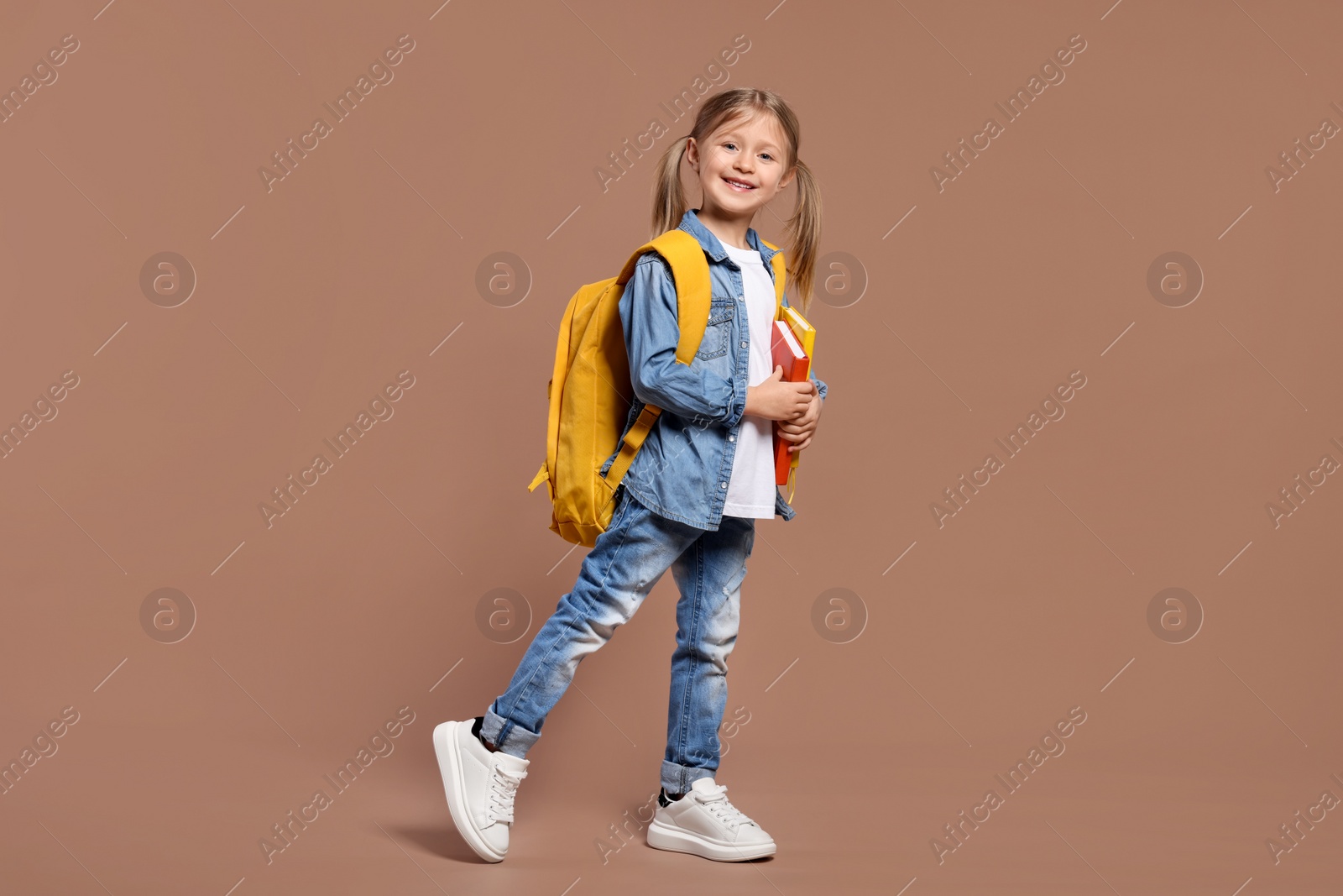 Photo of Happy schoolgirl with backpack and books on brown background