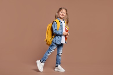 Happy schoolgirl with backpack and books on brown background