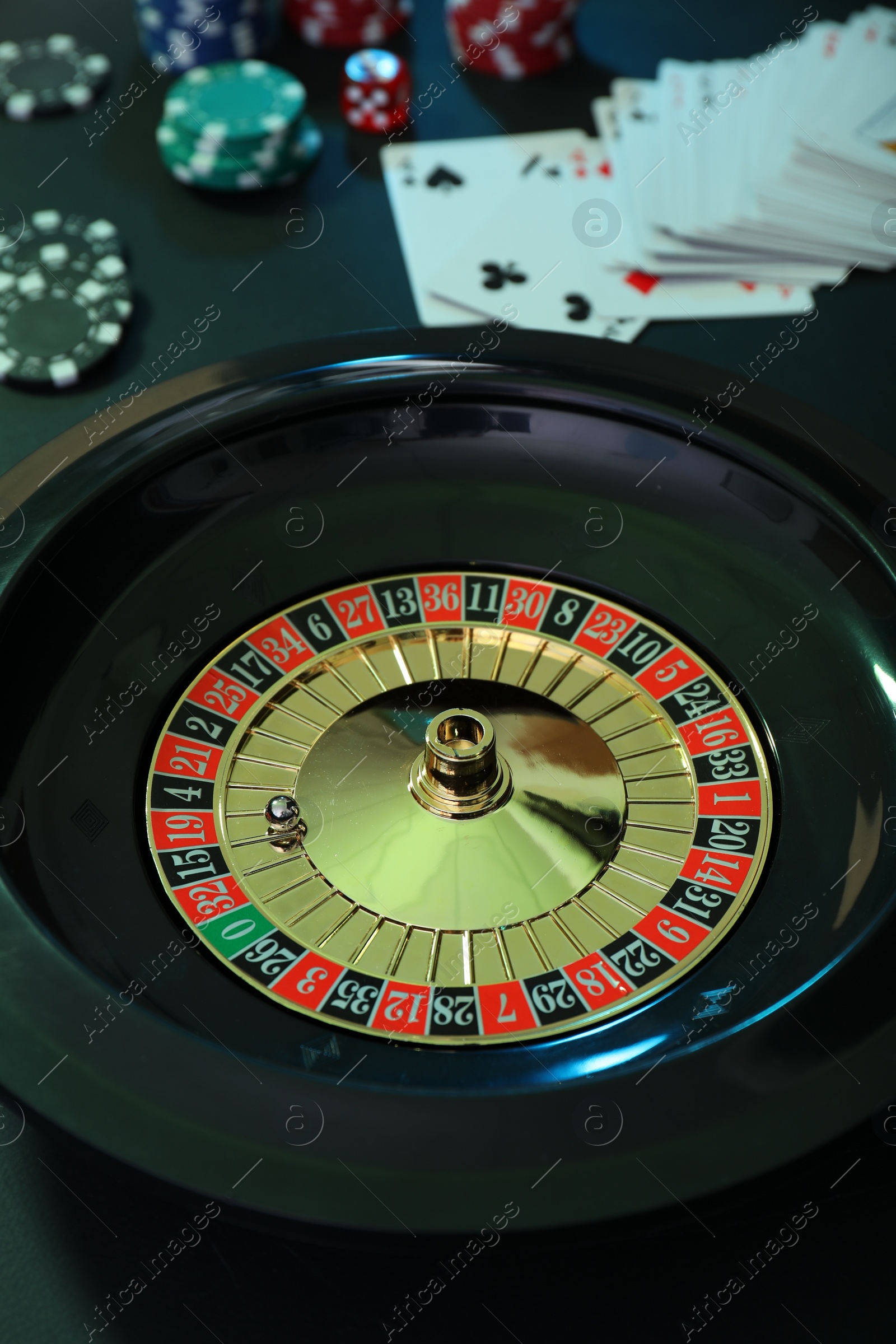 Photo of Roulette wheel, playing cards and chips on table, closeup. Casino game