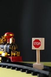 Road Stop sign as barrier blocking way for toy train on yellow surface, space for text. Development through obstacles overcoming