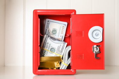 Photo of Open red steel safe with money and gold bars on shelf