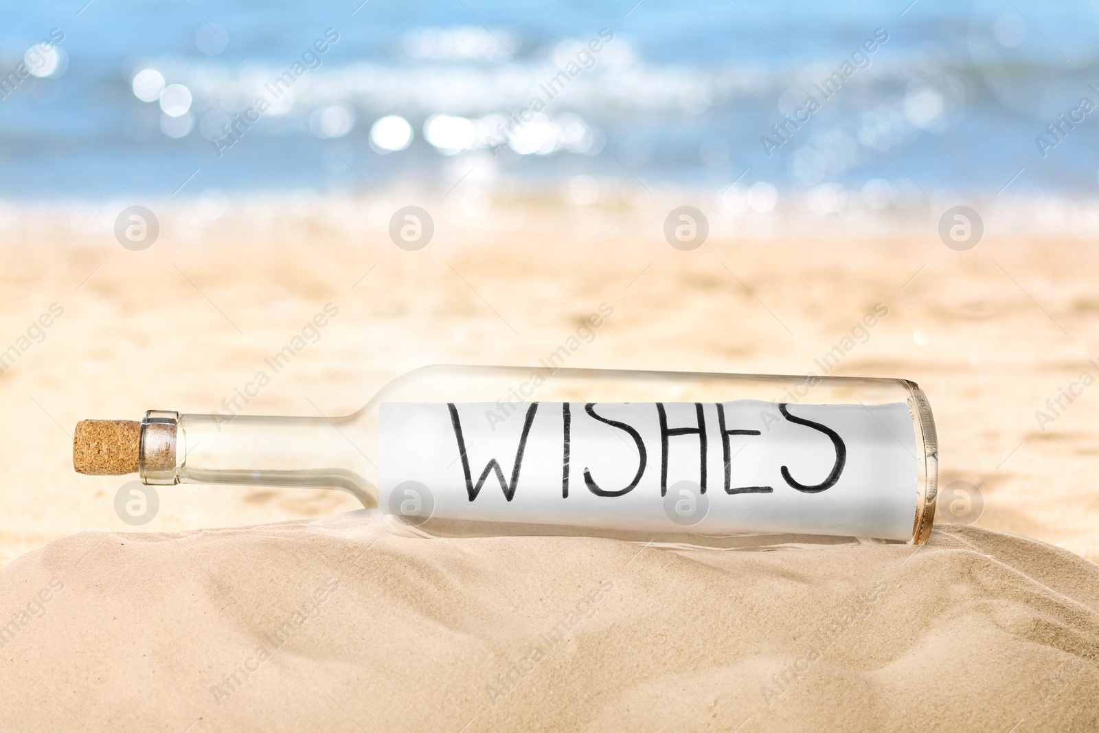 Image of Corked glass bottle with rolled paper note on sandy beach near ocean