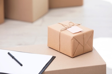 Photo of Clipboard and parcel with tag on cardboard box, indoors