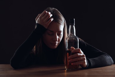 Photo of Alcohol addiction. Woman with bottle of whiskey at wooden table