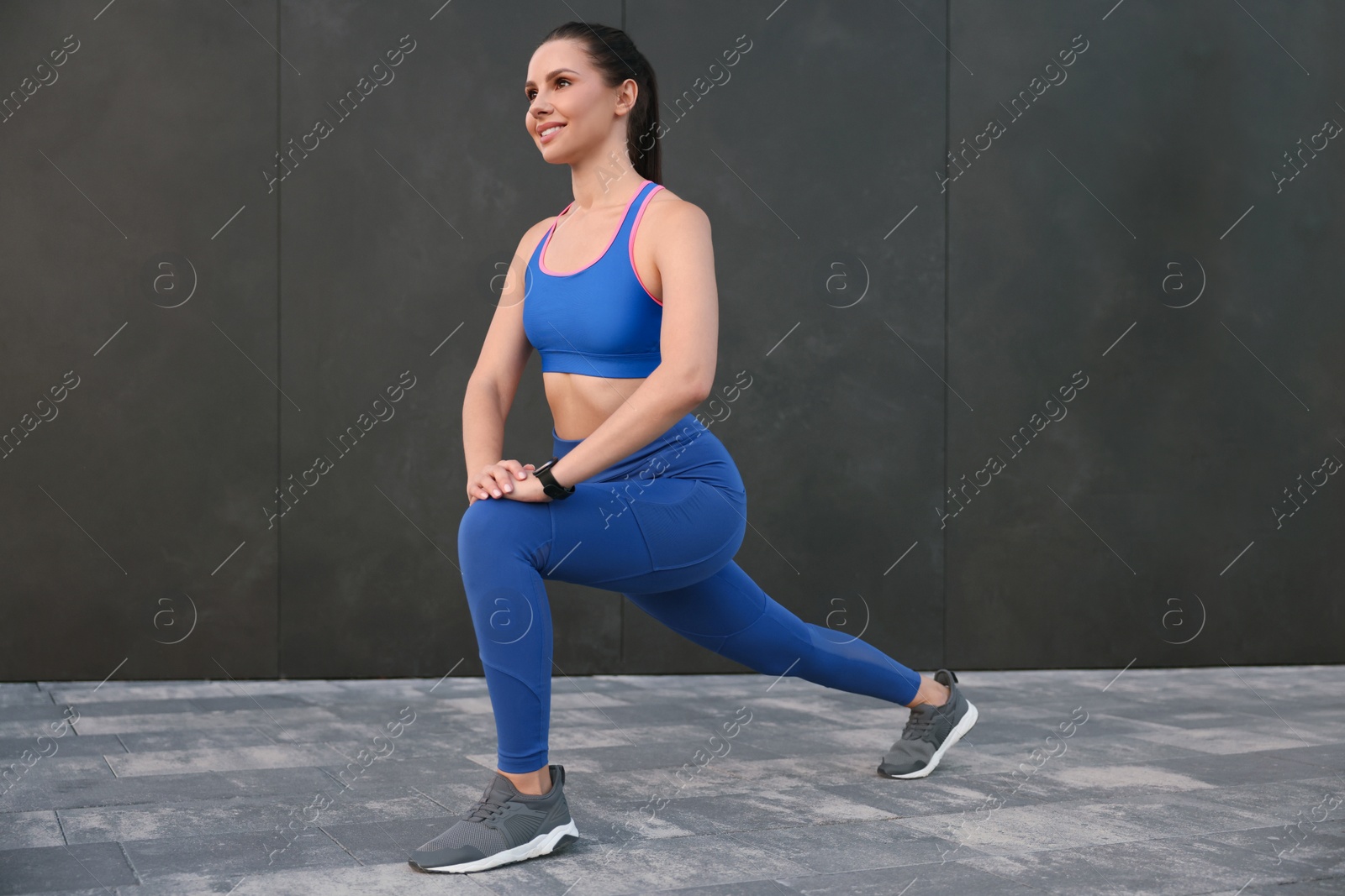 Photo of Beautiful woman in stylish sportswear doing exercises near black wall outdoors